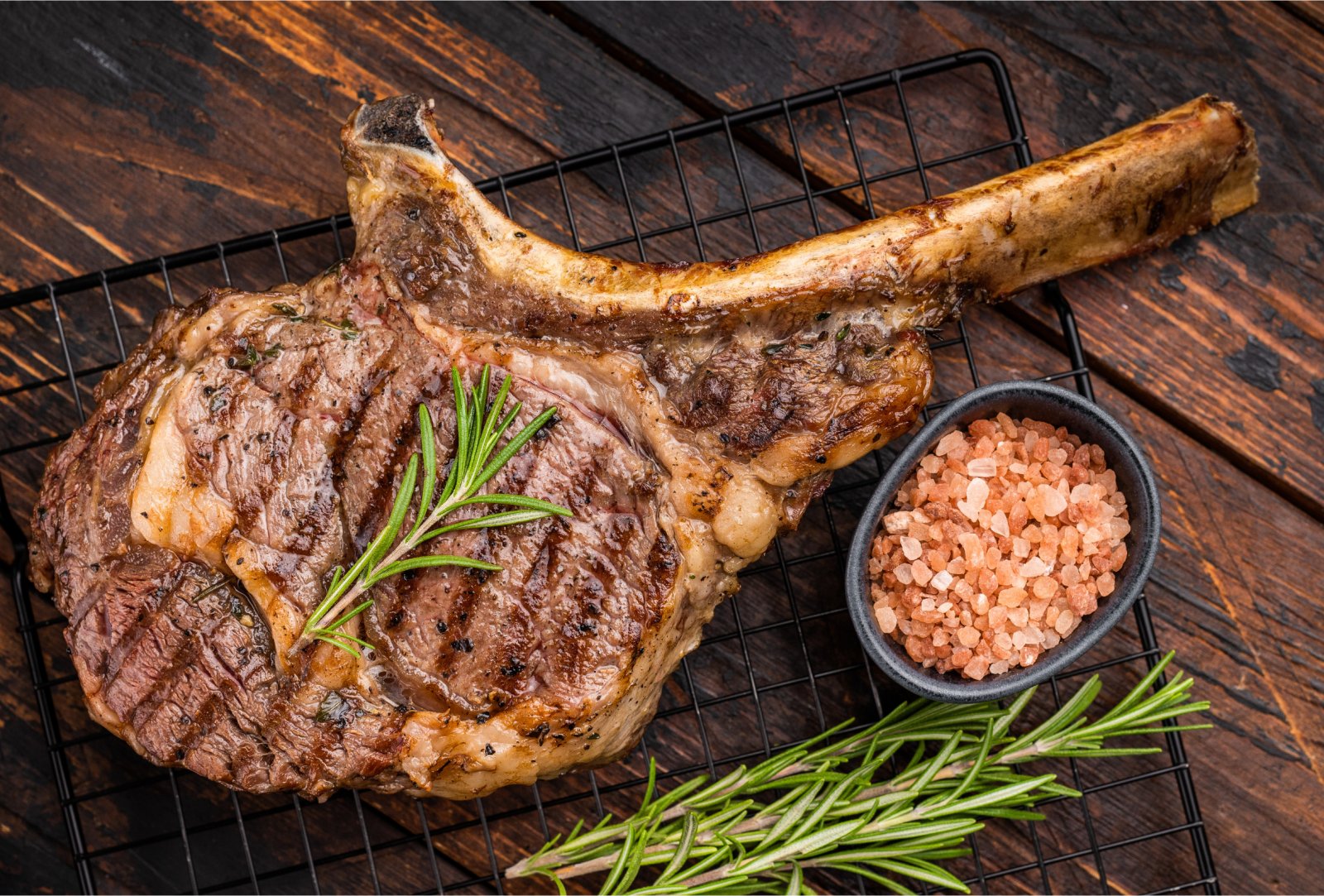 Cooked tomahawk steak on a wooden board with rosemary and salt