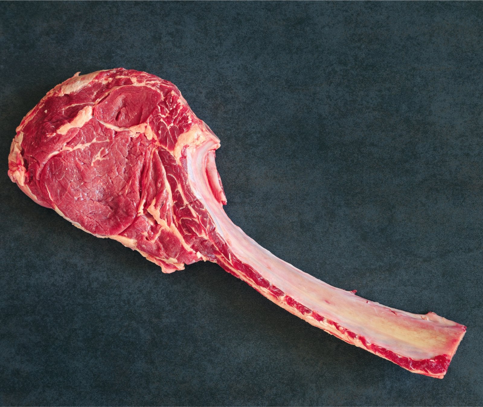 Raw tomahawk steak with the long rib bone on a dark slate